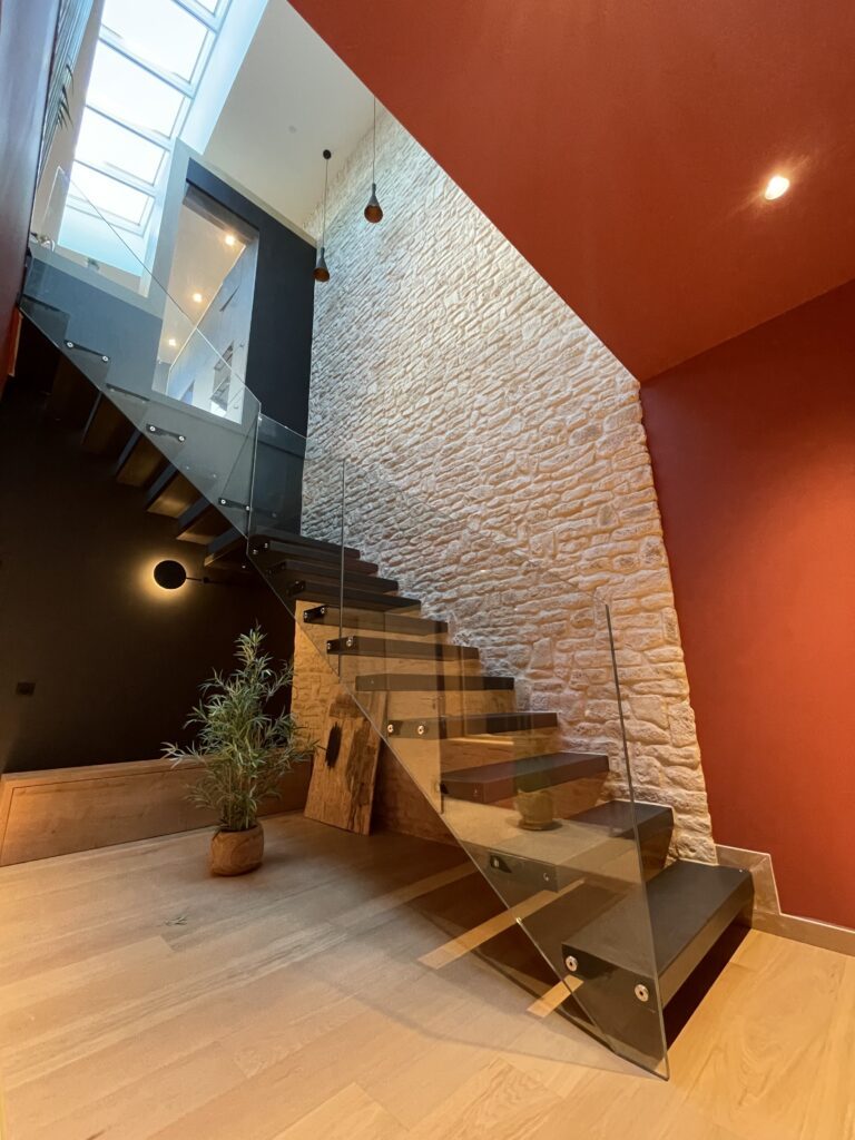 Escalier suspendu en bois et verre devant un mur de pierre, mur rouge